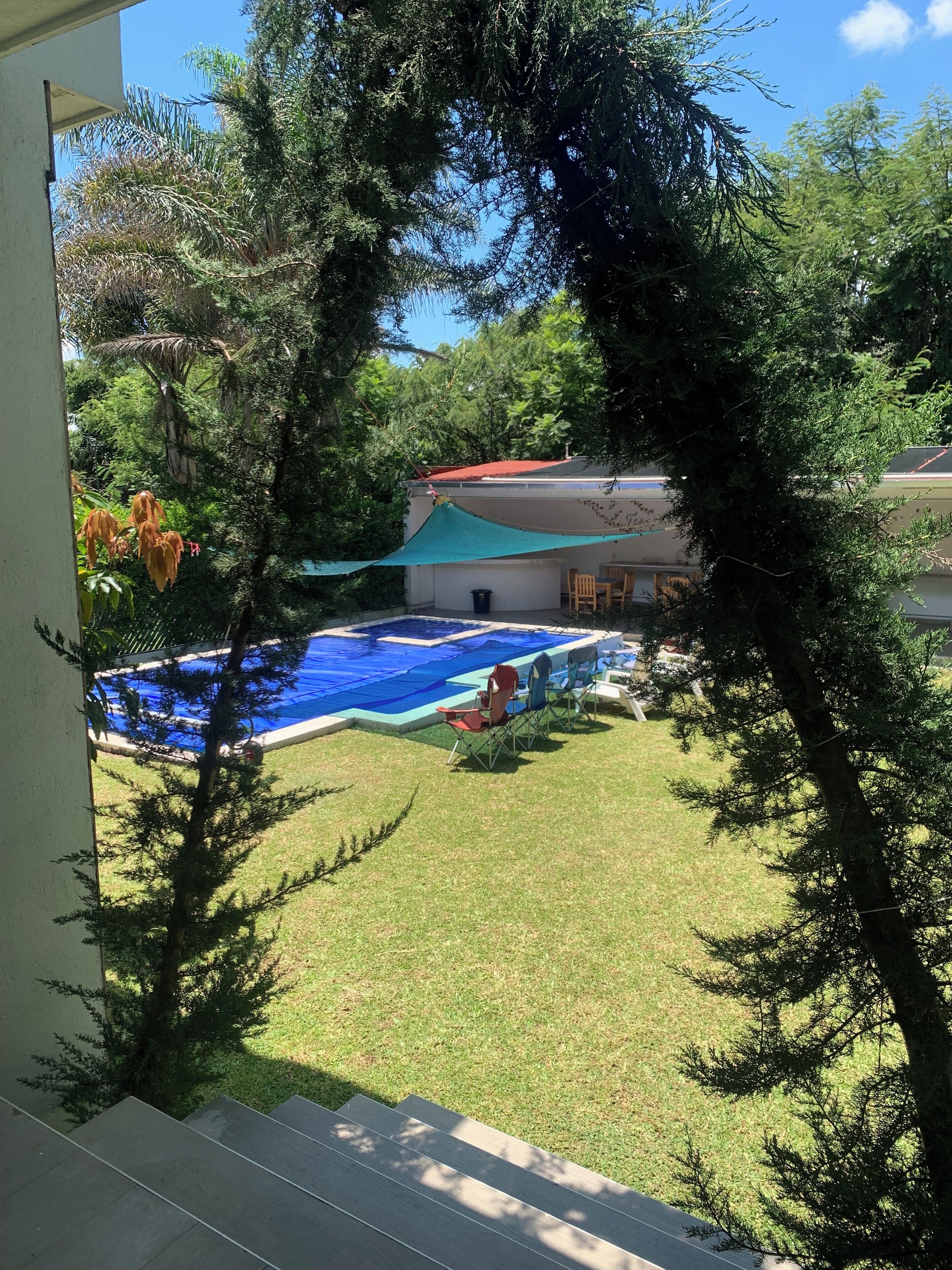 A backyard with a swimming pool, a covered patio, and a lawn.