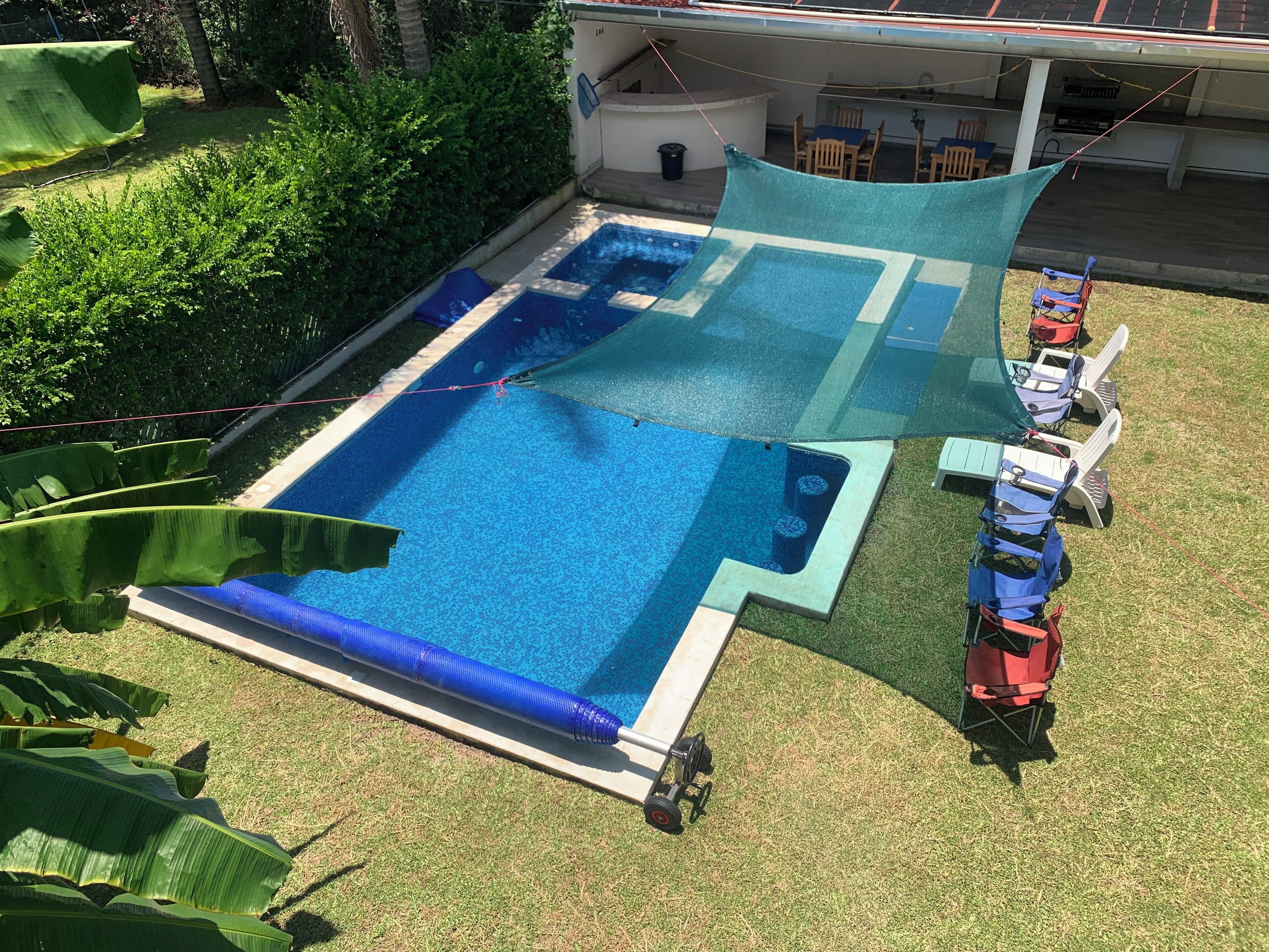 A rectangular swimming pool with a blue interior, surrounded by a grassy area and a shaded section.