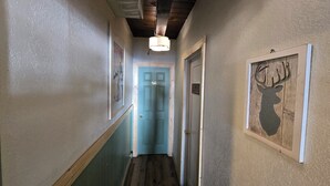 Un couloir avec une porte bleue, un plancher en bois et un ventilateur de plafond.
