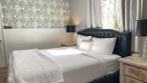 Un lit bien fait, avec du linge de lit blanc, une tête de lit noire en tissu et une table de chevet avec une lampe.