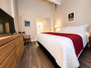 Ein Schlafzimmer mit einem Bett, einem Schminktisch, einem Sessel, einer Lampe und einem gerahmten Bild an der Wand.