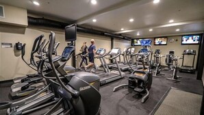 Un gimnasio con cintas de correr, elípticas y una pantalla de televisión.