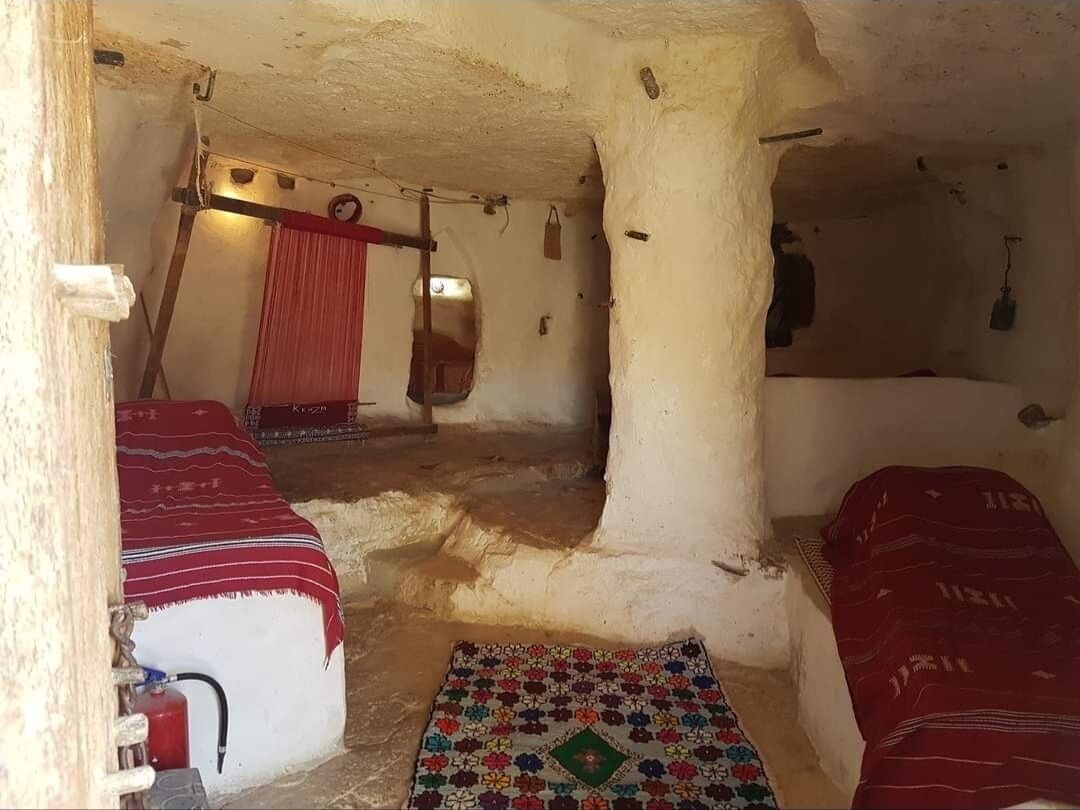 A room with two beds, a red curtain, a patterned rug, and a fire extinguisher.