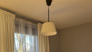 Un dormitorio con una cama, un ventanal con cortinas traslúcidas y una lámpara colgante.