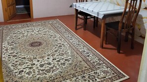 Un coin repas avec une table dressée pour deux personnes, un tapis à motifs et un mur orné d’un décor évoquant le marbre.