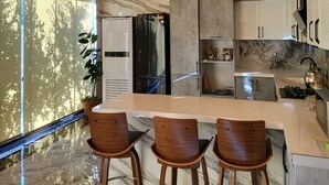 Une cuisine moderne avec un plafond en bois, un grand îlot central doté de tabourets de bar et une vue sur les arbres à travers de grandes fenêtres.