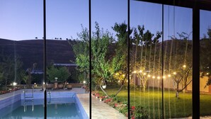 Une piscine dotée d’une terrasse carrelée, entourée d’un jardin aménagé avec des arbres et des fleurs, et offrant une vue sur un paysage vallonné.