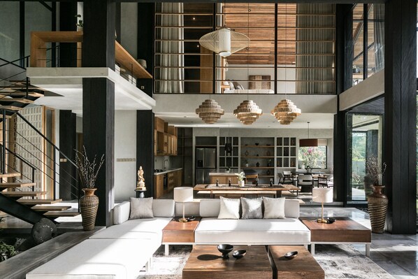 A modern interior with a central seating area, a staircase, and a kitchen in the background.