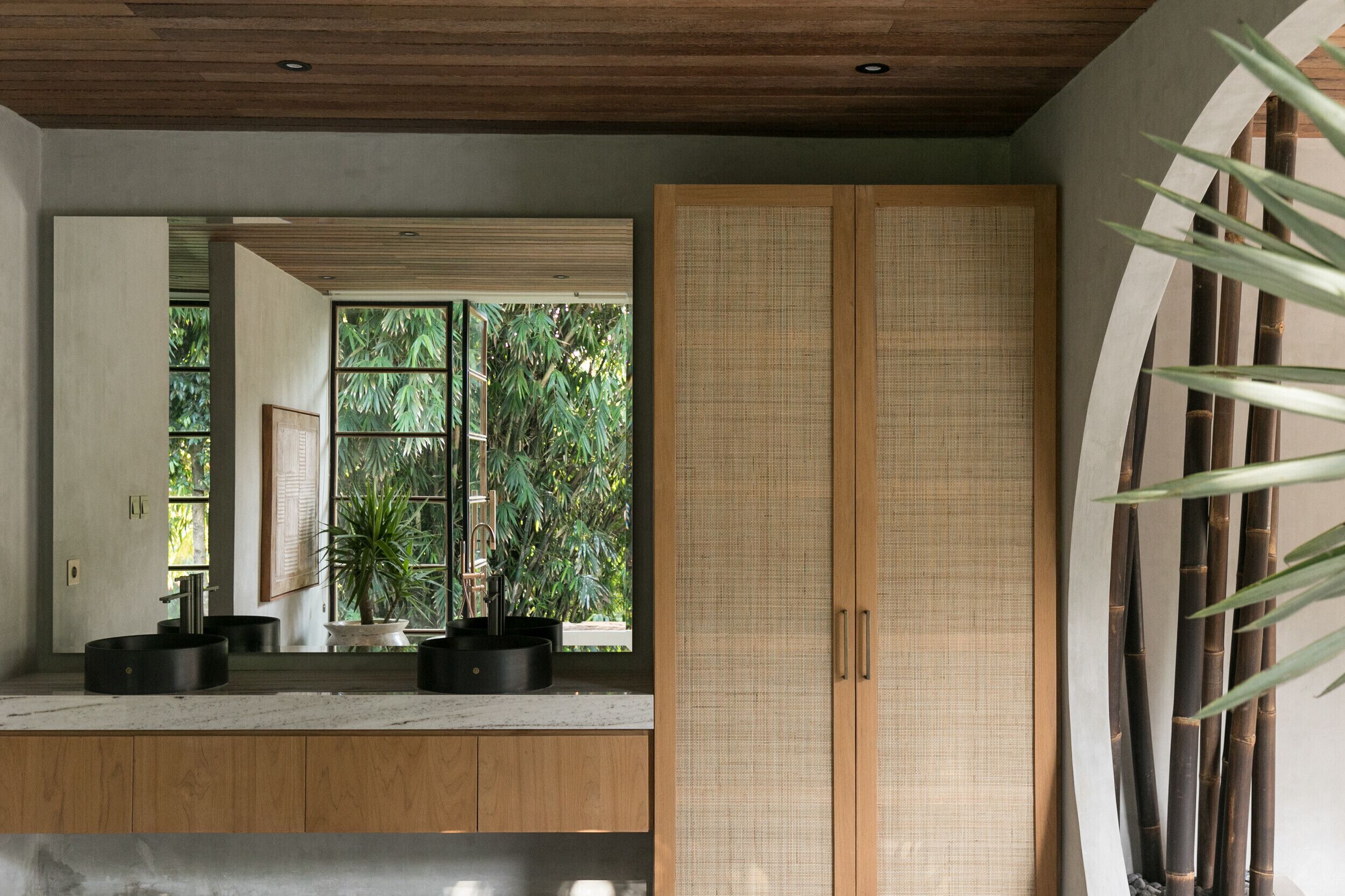 Une salle de bain moderne avec un meuble-lavabo en bois, un grand miroir et une vue sur la verdure à l’extérieur.