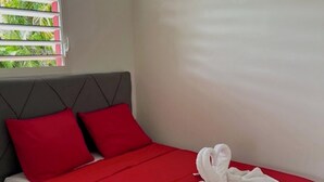 A bedroom with a bed, red bedding, and a towel on the bed. - BUNGALOW GRENADE (Saint-François)