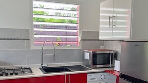 A modern kitchen with red cabinets, a stainless steel refrigerator, a washing machine, and a microwave. - BUNGALOW GRENADE (Saint-François)
