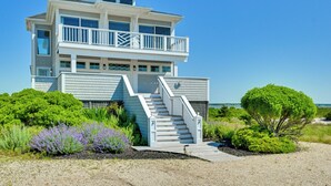 A multi-story beachfront house with a staircase leading to a balcony, surrounded by lush greenery and a clear sky. - Waterfront Westhampton Haven: Private Beach (Westhampton Beach)