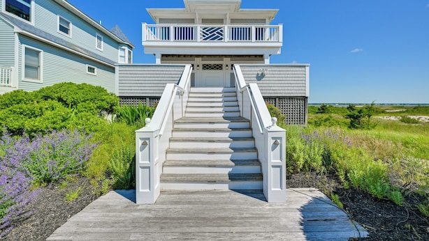 A two-story house with a balcony, a staircase leading to the entrance, and a view of the surrounding landscape. - Waterfront Westhampton Haven: Private Beach (Westhampton Beach)
