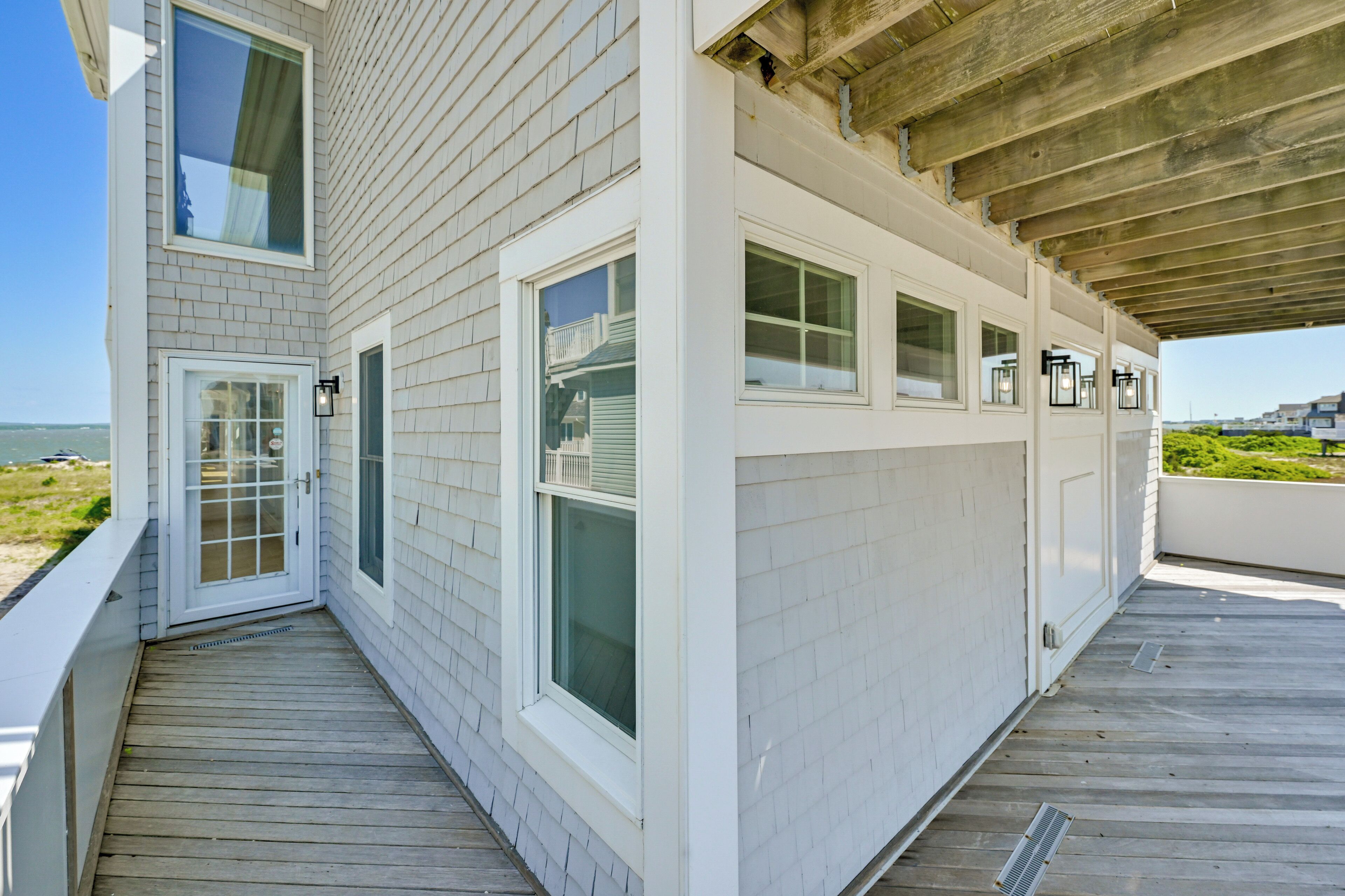 A coastal building with a wooden deck, large windows, and a covered area.