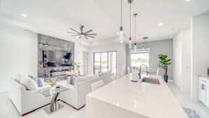 A modern kitchen with a central island, a dining area with a sofa, and a large window providing natural light. - Charming 4-bedroom house with Heated Pool (Cape Coral)