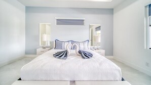 A spacious bedroom with a large bed, two nightstands, a mirror, and a window. - Charming 4-bedroom house with Heated Pool (Cape Coral)