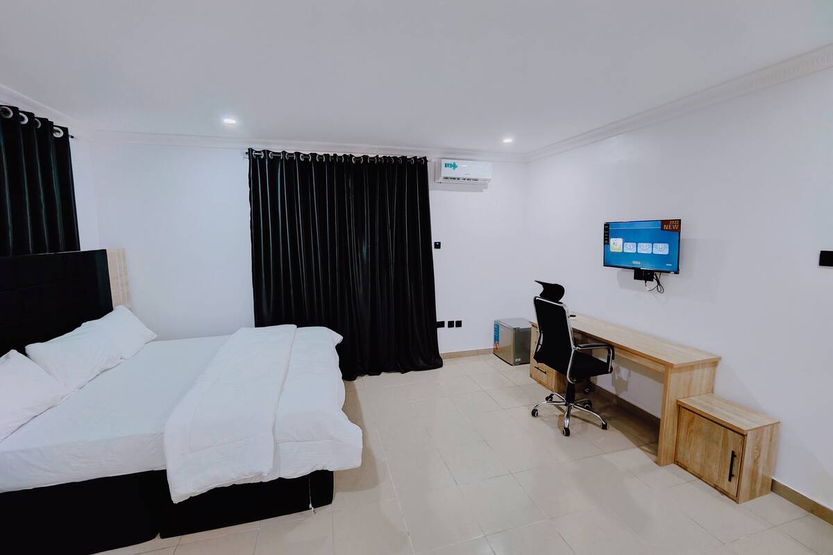 Ein Hotelzimmer mit Bett, Schreibtisch, Stuhl, Fernseher und einem kleinen Schrank.