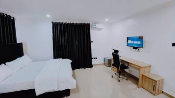 A hotel room with a bed, a desk, a chair, a television, and a small cabinet.