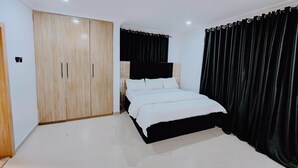 A bedroom with a bed, a wardrobe, and black curtains. - The Hub Apartment Lekki (Lekki)