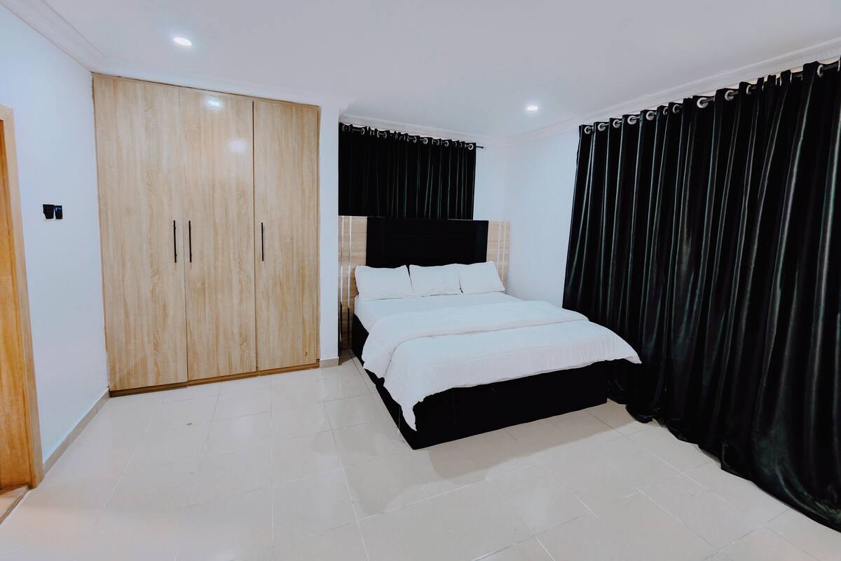 Ein Schlafzimmer mit einem Bett, einem Kleiderschrank und schwarzen Vorhängen.