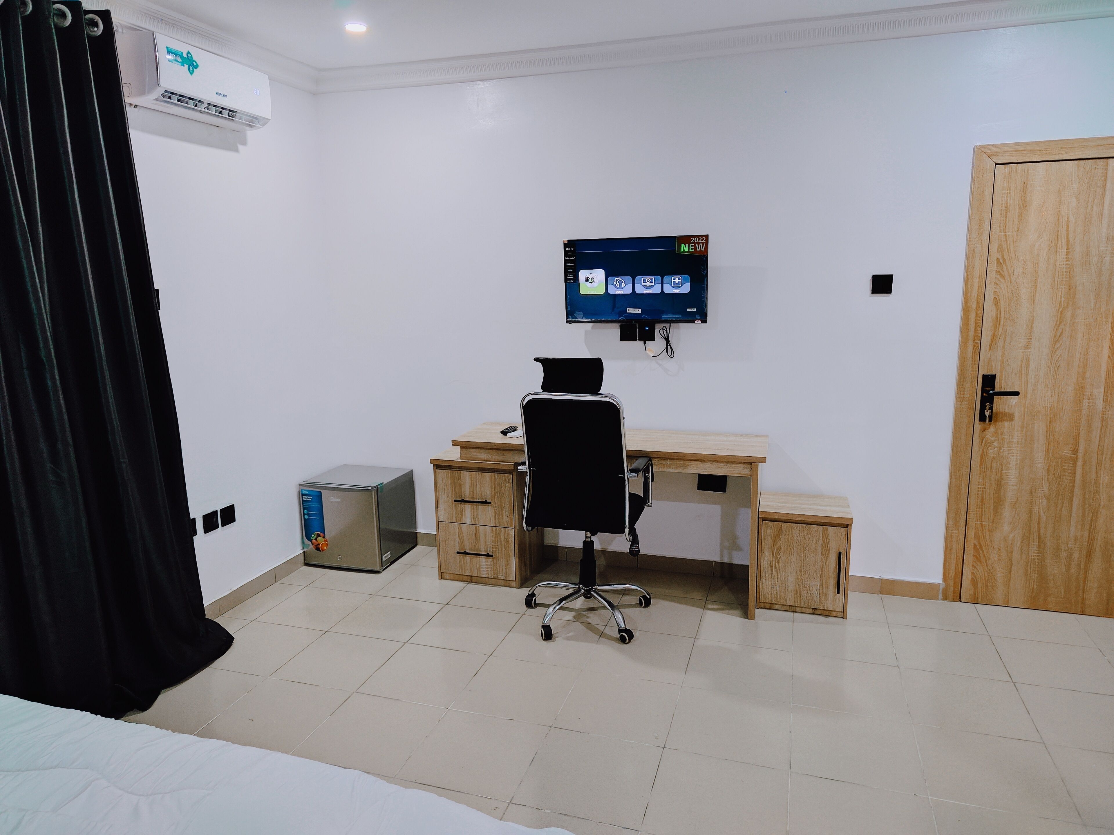 A hotel room with a bed, a desk with a chair, a TV mounted on the wall, and a wooden door.