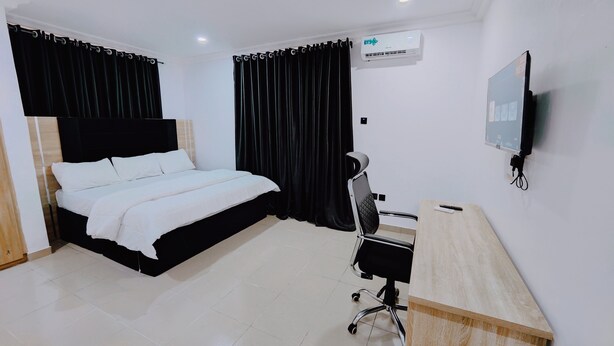 A hotel room with a bed, a desk, a chair, a TV, and an air conditioning unit. - The Hub Apartment Lekki (Lekki)
