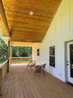 Eine Holzterrasse mit zwei Korbstühlen, einer weißen Außenwand und einer Tür mit Fenster.