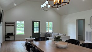 A spacious dining area with a long wooden table, black chairs, and a modern chandelier.