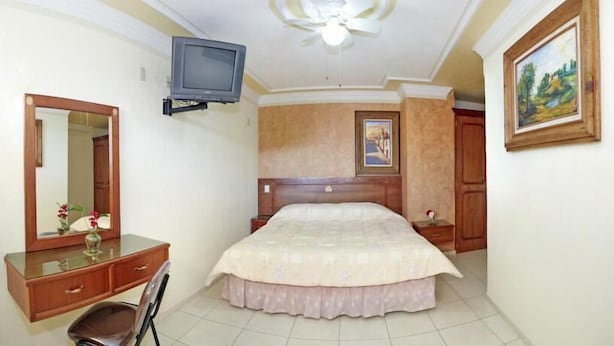 A bedroom with a bed, a dresser, a mirror, a television, and a painting on the wall. - Hotel Rincon Tarasco (Morelia)