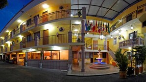 A multi-story hotel with balconies, a central fountain, and multiple flags. - Hotel Rincon Tarasco (Morelia)