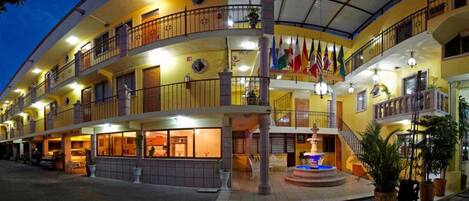 Un hotel de varios pisos con balcones, una fuente central y varias banderas.
