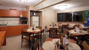 A dining area with round tables, chairs, and a kitchen in the background. - Hotel Rincon Tarasco (Morelia)