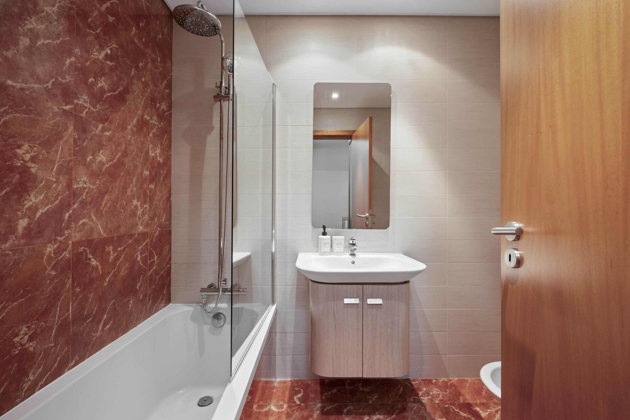 A modern bathroom with a glass-enclosed shower, a white sink with a mirror above it, and a wooden door.