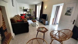 Una sala de estar con un sofá, dos sillones de mimbre, una mesa de centro, un televisor y una estantería.
