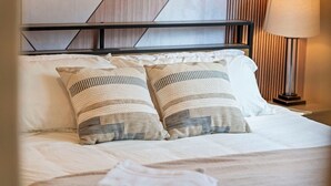 Un lit bien fait, avec deux coussins à motifs et une tête de lit ornée d’un motif géométrique.
