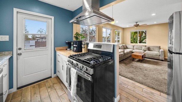 Une cuisine moderne équipée d’une cuisinière, d’un four et d’une hotte en acier inoxydable. On y trouve également un coin repas avec un canapé et une table basse.