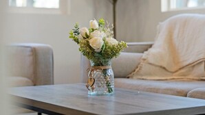 Ein Wohnzimmer mit freiem Blick, ein beiges Sofa, eine Glasvase mit weißen Blumen auf einem Holztisch.