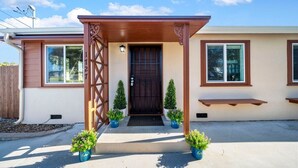 Ein Haus mit einer Holzveranda, einer dunklen Haustür und je einem kleinen Topfpflanzen auf jeder Seite.