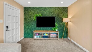 Une pièce avec un mur vert à texture, un téléviseur à écran plat fixé au-dessus d’une console en bois, une lampe et une porte.