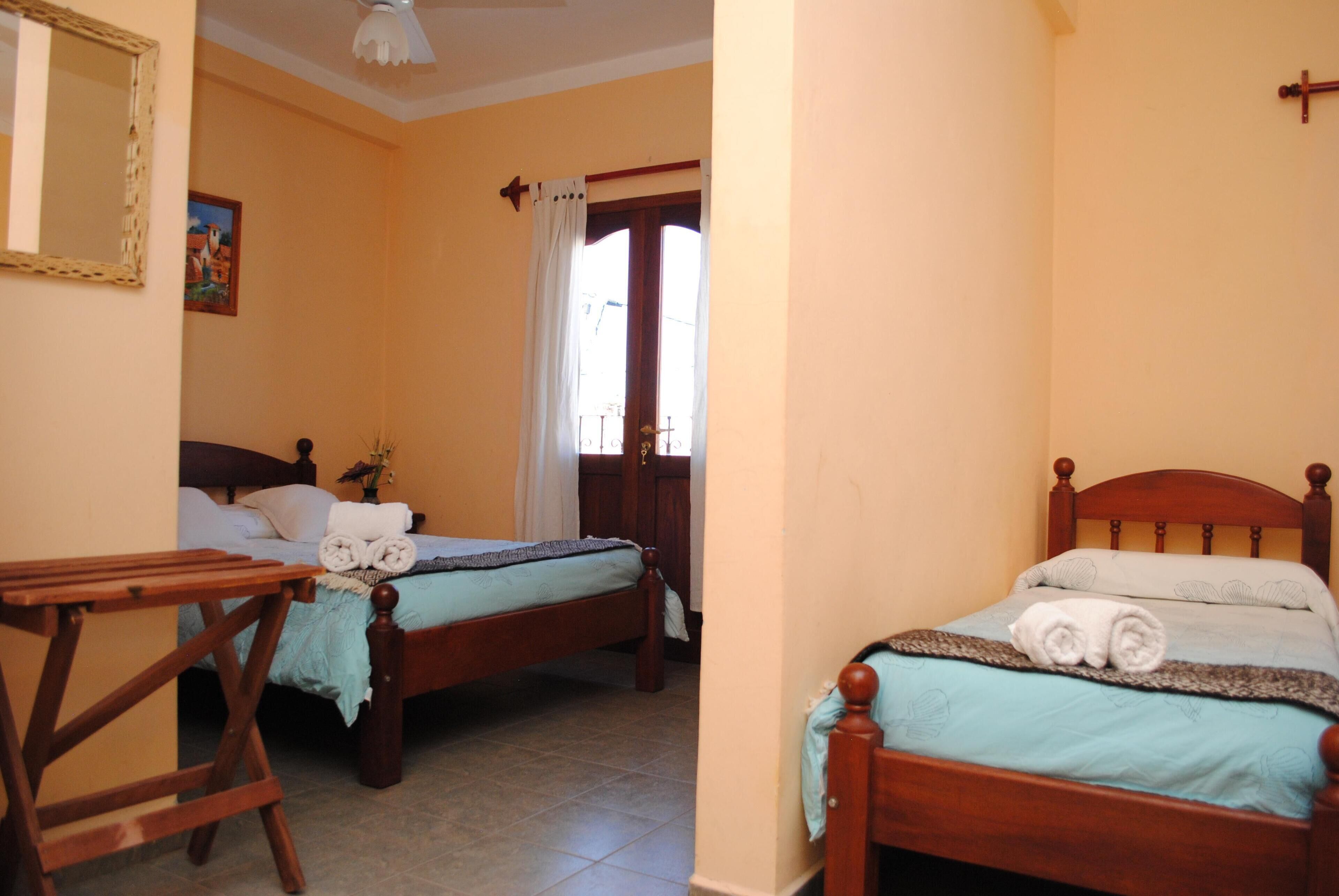 A room with two wooden beds, a wooden table, and a mirror on the wall.