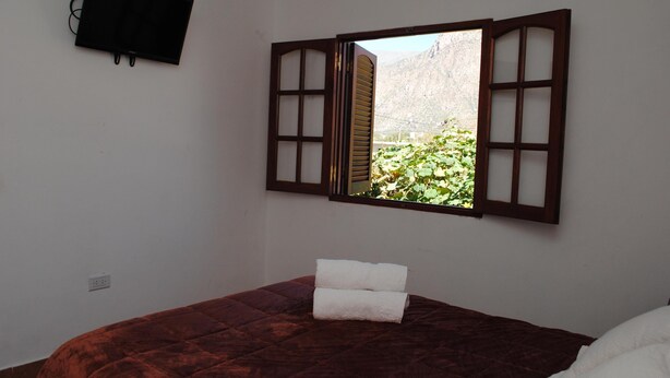 Une chambre avec un lit, une fenêtre dotée de volets en bois, un téléviseur à écran plat fixé au mur et une vue sur la verdure.