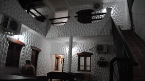 Une pièce faiblement éclairée, avec une table et des chaises en bois rustique, un escalier en briques et des murs blancs à la texture particulière.