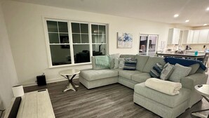 Un salon moderne avec un canapé d’angle, une petite table basse et un coin repas comprenant une table et des chaises blanches.