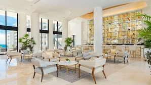 A spacious lobby with a bar area, seating arrangements, and large windows offering a view of the sea.