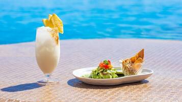 A glass of a creamy beverage with a garnish, a plate with a salad and a folded item, and a pool in the background.