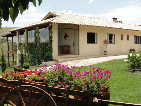 A house with a large glass door, a patio with potted plants, and a grassy lawn. - Pousada Morro Verde (Águas de Lindóia)