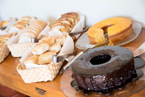 A variety of baked goods including bread rolls, a cake, and a chocolate dessert on a wooden table. - Pousada Morro Verde (Águas de Lindóia)