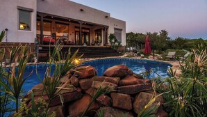 A modern house with a swimming pool surrounded by rocks and plants. - Resort Style S/W Home on 3 Acres. Views, Pool, Outdoor Fireplace (Bulverde)