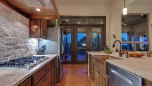 A modern kitchen with a stone wall, wooden cabinets, and a stainless steel dishwasher. - Resort Style S/W Home on 3 Acres. Views, Pool, Outdoor Fireplace (Bulverde)