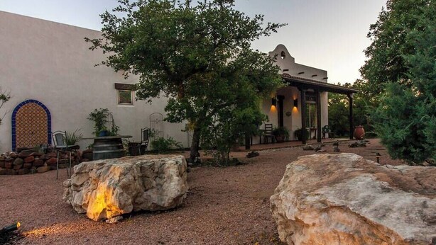 A courtyard with a stone fountain, large rocks, and a building with a tiled entrance. - Resort Style S/W Home on 3 Acres. Views, Pool, Outdoor Fireplace (Bulverde)